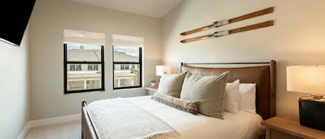Un dormitorio con una cama, dos mesitas de noche, una lámpara de noche, una ventana con vistas y un perchero de esquíes en la pared.