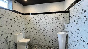 A bathroom with a white toilet, a sink, and a shower. The walls have a speckled pattern. - Coastal Palm (Alibag)