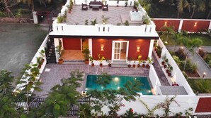A modern building with a swimming pool, surrounded by lush greenery and palm trees. - Coastal Palm (Alibag)