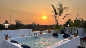 A rooftop jacuzzi with a sunset view, surrounded by potted plants and a street lamp. - Coastal Palm (Alibag)