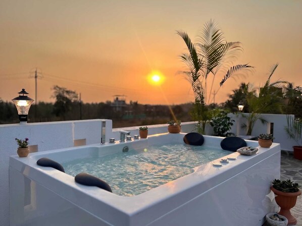 A rooftop jacuzzi with a sunset view, surrounded by potted plants and a street lamp. - Coastal Palm (Alibag)