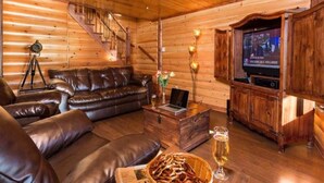 A log cabin interior with a leather sofa, a wooden entertainment center, and a staircase. - Hôtel à la maison - Le repère du Massif avec spa! (Petite-Rivière-Saint-Fran çois)
