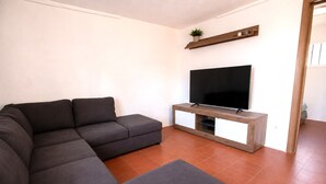 Un soggiorno moderno con un divano componibile, una TV a schermo piatto su un mobile in legno e una piccola pianta su uno scaffale.