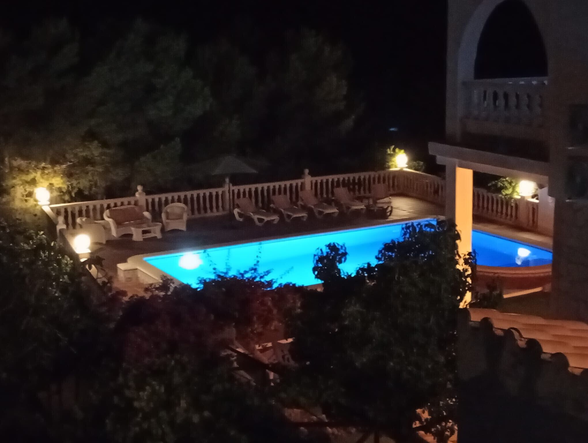 Vista noturna de uma piscina com espreguiçadeiras e uma área de estar coberta.