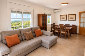 A living room with a grey sectional sofa, a dining table with chairs, a wooden cabinet, and two framed pictures on the wall. - Spacious Mountain Retreat with Private Pool (La Bisbal del Penedés)