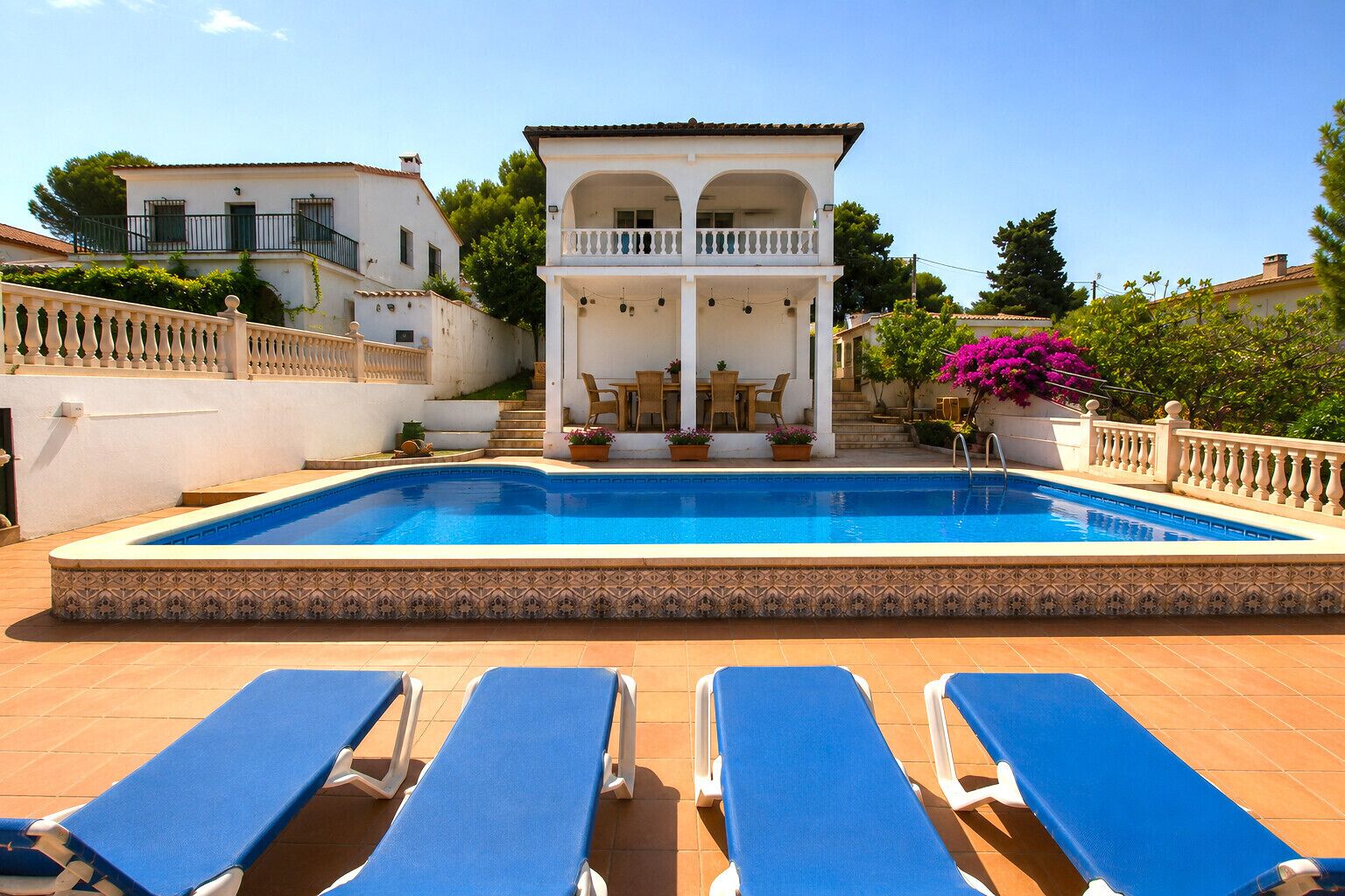 A swimming pool with blue lounge chairs and a covered seating area.