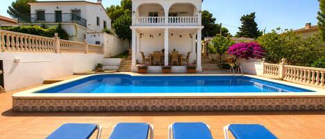 A swimming pool with blue lounge chairs and a covered seating area.