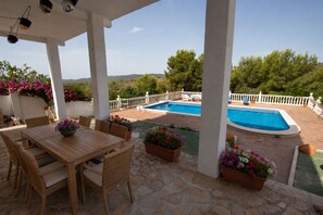 A covered outdoor area with a pool, stone flooring, wicker furniture, and potted plants. - Spacious Mountain Retreat with Private Pool (La Bisbal del Penedés)