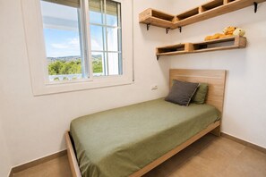 A single bed with a green bedspread, a window with a view, and wooden shelves above the bed. - Spacious Mountain Retreat with Private Pool (La Bisbal del Penedés)