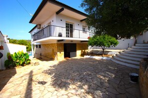 A two-story building with a balcony, stone paving, and a small tree.