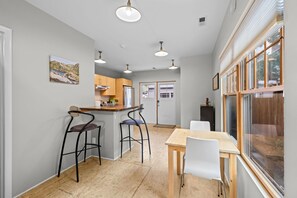 A compact kitchen with a dining area, bar stools, and a view through large windows. - New! Private Carriage House | Walk to Broadway Shops & Restaurants (Denver)