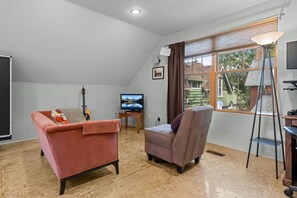 A living room with a pink sofa, a purple armchair, a guitar, a TV, and a window with blinds. - New! Private Carriage House | Walk to Broadway Shops & Restaurants (Denver)