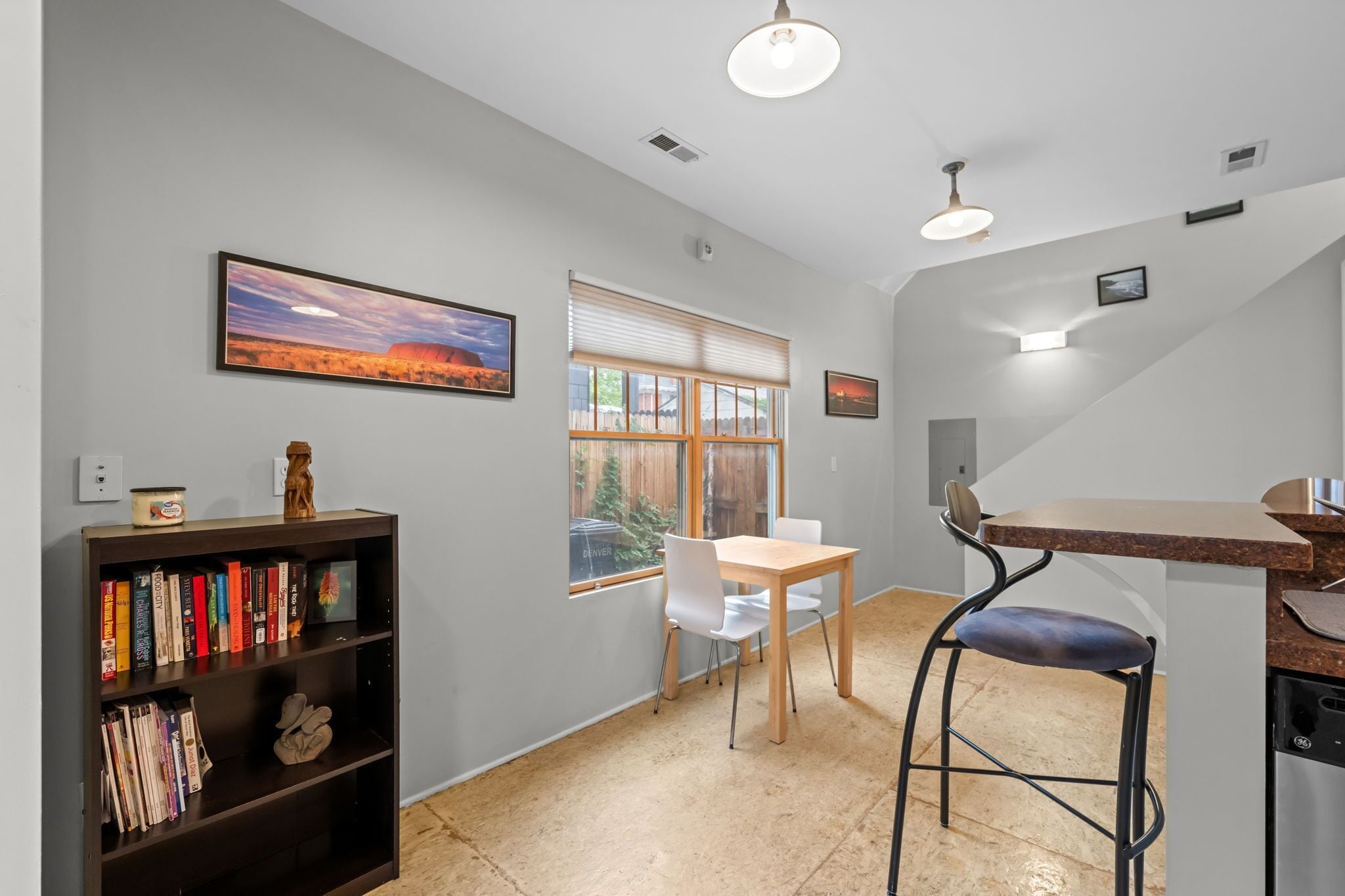 A modern kitchen with a dining area, a bookshelf, and a window with a view of a building.
