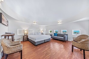 A modern bedroom with a curved ceiling, a large bed, a sofa, two wicker chairs, and a desk with a lamp. - Whitsunday Blue Penthouse (Airlie Beach)