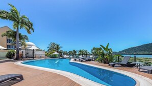 Ein Swimmingpool mit Liegestühlen und Palmen, umgeben von einer Holzterrasse und einem Gebäude mit einer Kuppel.