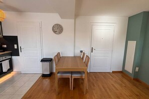 A dining area with a wooden table and chairs, a clock on the wall, and white doors. - Cath' Home - Studio on Place de la Cathédrale (Colmar)