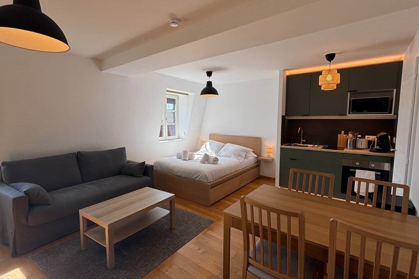 Ein kompakter Wohnraum mit einer Couch, einem Bett, einem Esstisch und einer Küchenzeile.