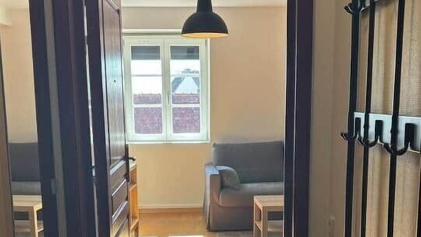 Ein Flur, der in einen Wohnbereich mit einer Bank, einer Pendelleuchte und einem Kleiderhaken führt.