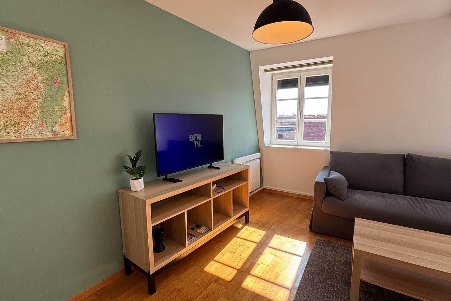 A living room with a television on a wooden stand, a sofa, a window with blinds, and a map on the wall.