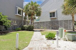 Un camino conduce a una zona vallada con un letrero que dice 'NO GOLF CARTS', rodeada de follaje y un edificio con fachada metálica.