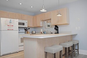 Una cocina con armarios de madera, un refrigerador blanco, un microondas, una estufa y una barra con taburetes.