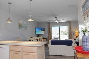 A modern kitchen with a central island, dining area with chairs, a television, and a view of the outdoors. - 🌊Coastal Townhouse | Pool & Tennis Court | Walk2Beach | Barrier Dunes 542 - 55 (Cape San Blas)