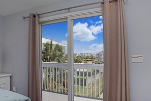 Una habitación con un ventanal grande, una cama blanca y vistas a un área exterior cercada con vegetación.