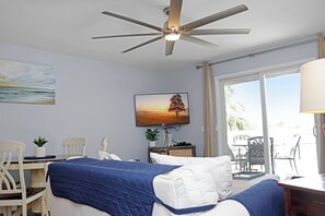 Ein Hotelzimmer mit einem Bett, einem Schreibtisch, einem Stuhl, einem Deckenventilator, einem Fenster und einem Bild an der Wand.