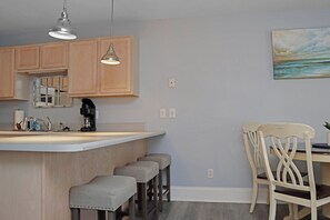 A kitchen with wooden cabinets, a bar area with stools, and a painting on the wall. - 🌊Coastal Townhouse | Pool & Tennis Court | Walk2Beach | Barrier Dunes 542 - 55 (Cape San Blas)
