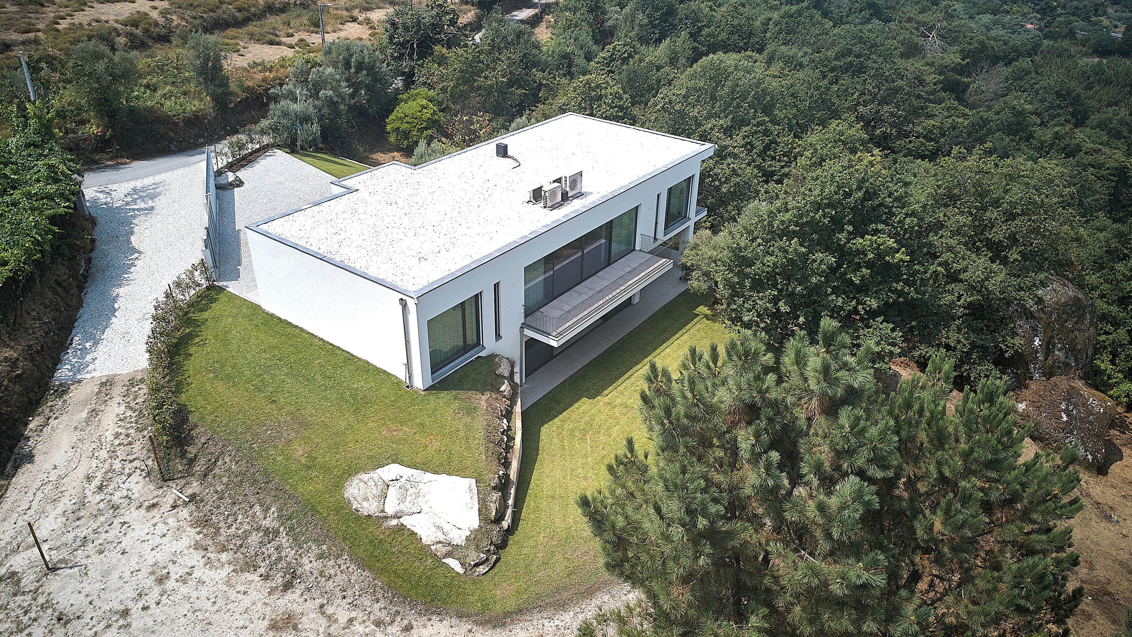 Una moderna casa a due piani con tetto piatto, ampie finestre e vialetto pavimentato.