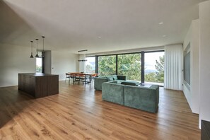 Ein geräumiger Wohnbereich mit Holzboden, einer Sitzecke mit grünen Sofas, einem Esstisch mit Stühlen und einer Kücheninsel.