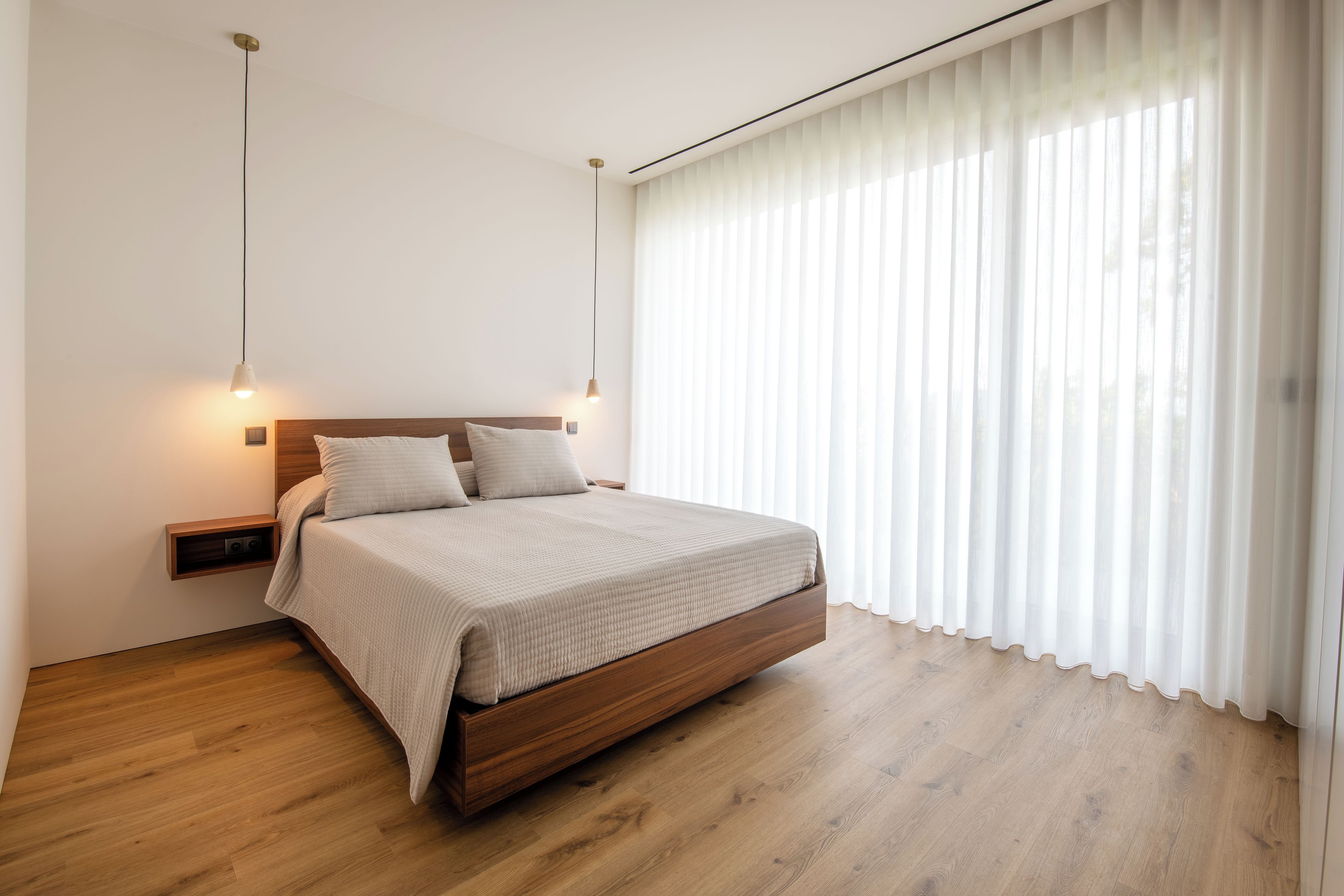 Een moderne slaapkamer met een houten bed, wit beddengoed en dunne gordijnen.