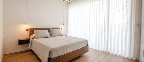 A modern bedroom with a wooden bed, white bedding, and sheer curtains.