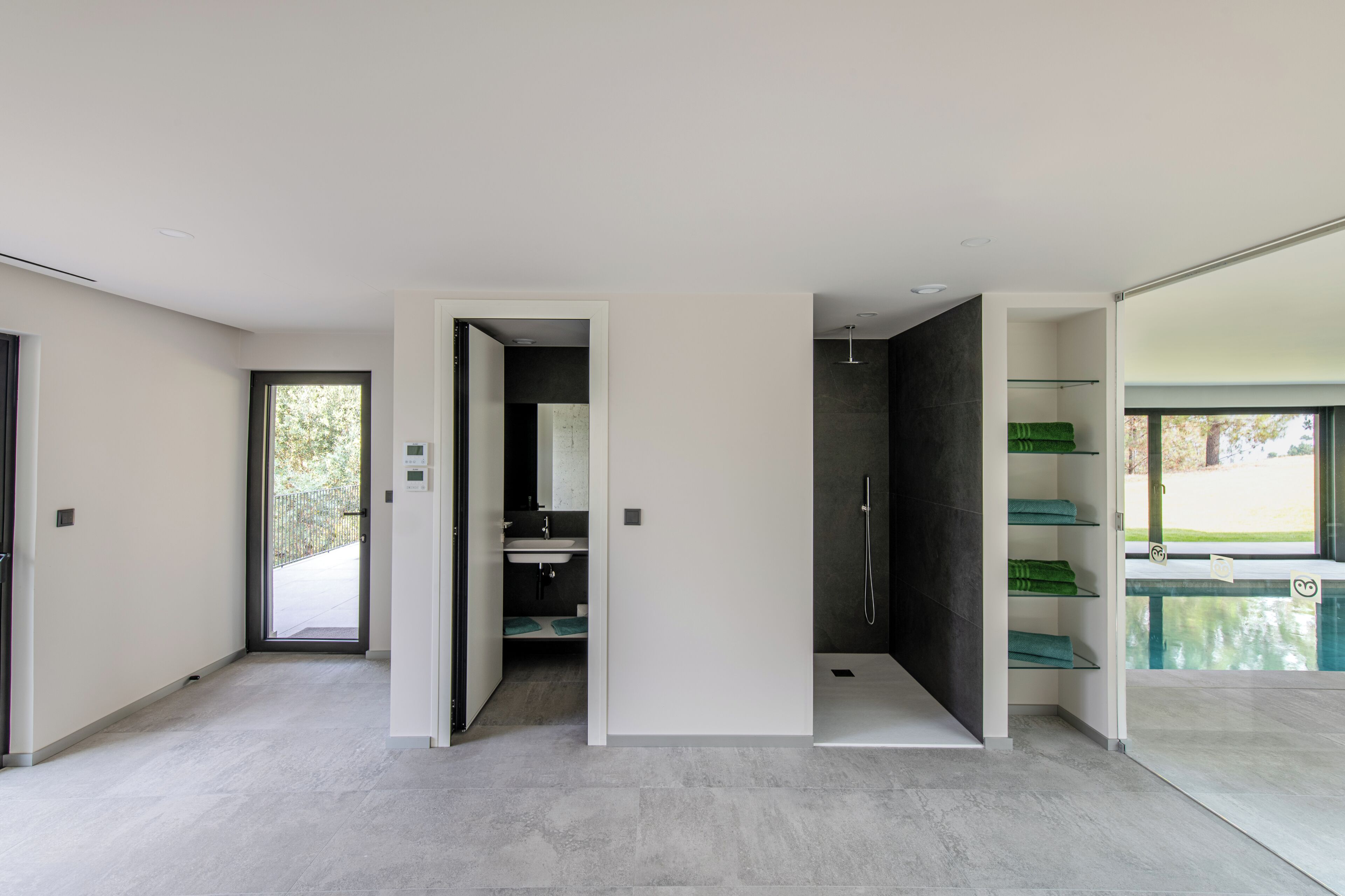 A modern bathroom with a shower, a sink, and a toilet. There is a glass door leading to a pool area.