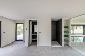 Ein modernes Badezimmer mit Dusche, Waschbecken und Toilette. Eine Glastür führt zu einem Poolbereich.