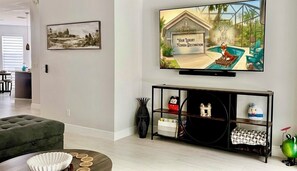 Un saló amb televisió de pantalla plana, un sofà verd, una taula consola amb objectes decoratius i un quadre al mur.