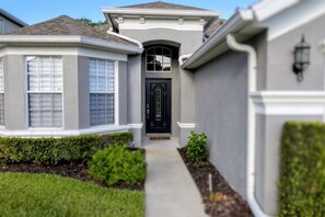 A residential house with a front entrance, a covered porch, and a pathway leading to the door. - Peaceful & Modern Retreat - Pool & Themed Rooms! (Davenport)