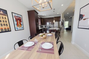 A modern kitchen with dark cabinets, a central island, and a dining area with a long table set for four. - Peaceful & Modern Retreat - Pool & Themed Rooms! (Davenport)