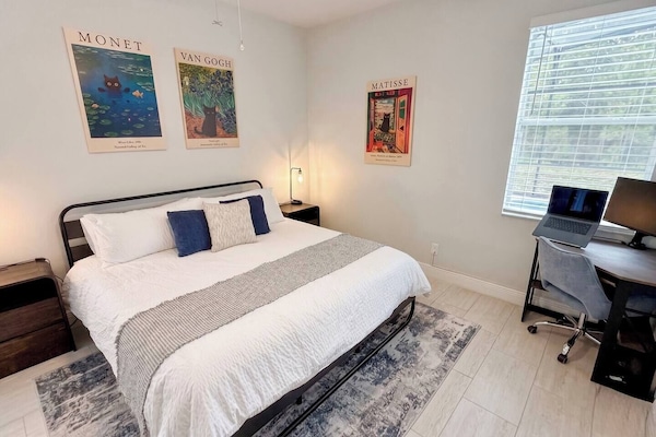 Bedroom 1: King Bed with ceiling fan, wall-mounted TV, corner workstation, closet, and en-suite bathroom with soaking tub and shower. Windows overlook pool and conservation area.