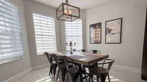 Uma sala de jantar com uma mesa retangular, seis cadeiras, um candelabro e duas imagens emolduradas na parede.