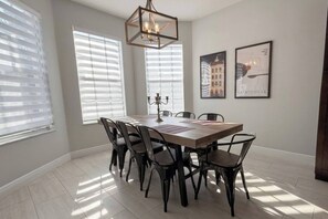 A dining room with a rectangular table, six chairs, a chandelier, and two framed pictures on the wall. - Peaceful & Modern Retreat - Pool & Themed Rooms! (Davenport)