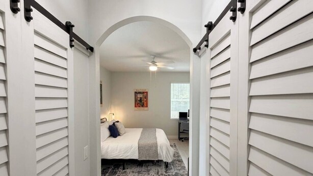Quarto com cama, escrivaninha e ventilador de teto.