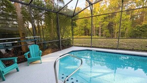 Uma piscina ao ar livre com estrutura de vidro, cercada por árvores e equipada com escada de metal.