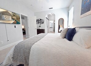 Un dormitorio con una cama grande, un televisor montado en la pared y una puerta que da a otra habitación.