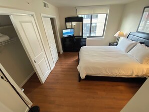 A bedroom with a bed, a dresser, a TV, and a window. - Furnished 1-bedroom apartment in Arlington with garage onsite parking included (Arlington)