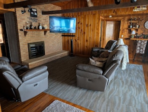 A cozy living room with a fireplace, leather recliners, a flat-screen TV, and wooden paneling. - Escape to the Lake- Cozy Lakefront Family Retreat (National City)