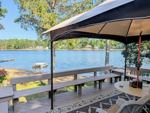 A covered outdoor deck with benches and a table, overlooking a calm lake with docks and houses in the background. - Escape to the Lake- Cozy Lakefront Family Retreat (National City)
