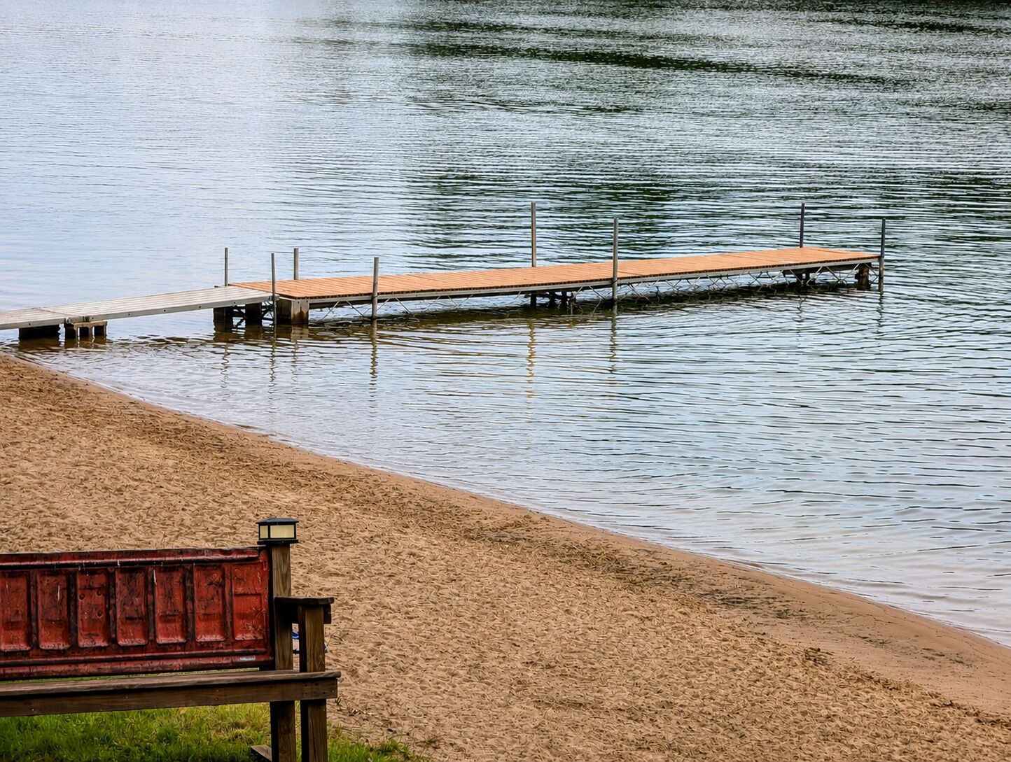 A wooden pier extending into calm water, a sandy beach, and a bench.