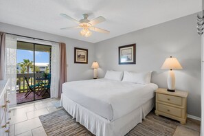 Habitación de hotel con cama, dos lámparas de noche, ventilador de techo, ventana con cortinas y vistas al exterior.