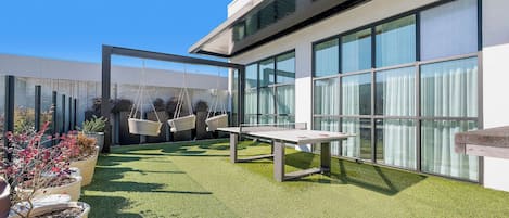 A modern outdoor area with a table and chairs, surrounded by potted plants and a glass wall.